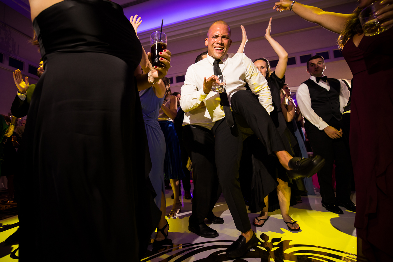 fun, unique image of guests as they dance during this palace at somerset wedding reception as purple and yellow lights flash around them 