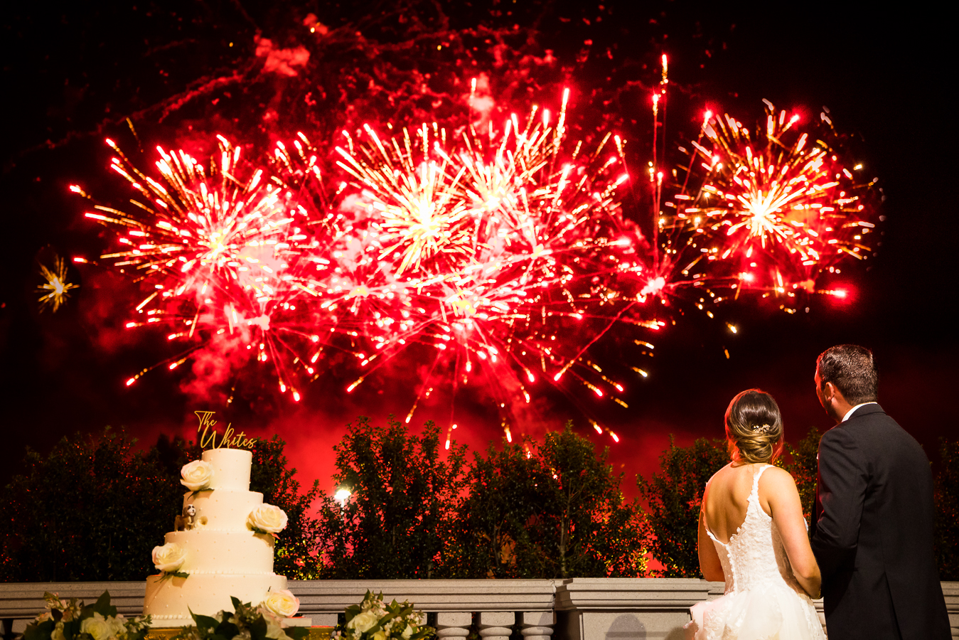 fun, vibrant colorful image of the red firework display that was set off during this black and gold wedding reception as the bride and groom watch in awe of the display outside of the palace at somerset park in NJ 