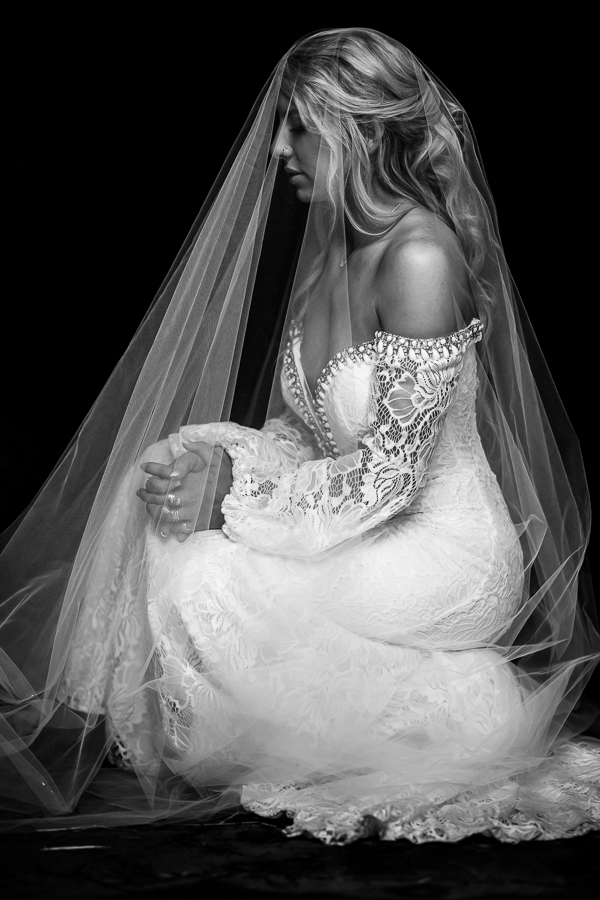 best pa wedding photographer, lisa rhinehart, captures this black and white image of the bride as she kneels down with her veil over her head and prays before her country wedding ceremony in halifax pa