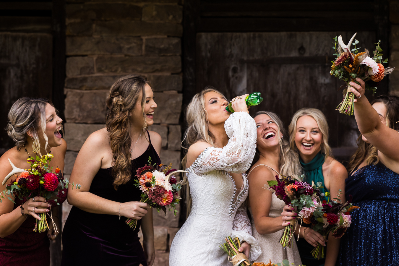 fun, unique, candid image of the bride as she chugs Mountain Dew while her bridesmaids cheer her on and laugh during their wedding party pictures