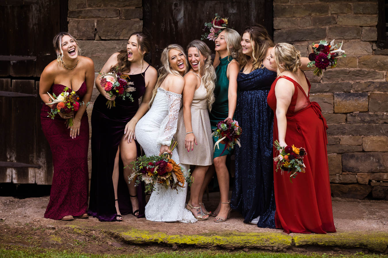pa country wedding photographer, lisa rhinehart, captures this fun, candid, unique bridal party portrait of the bride with her bridesmaids who are dressed in all different colored and styled dresses holding their vibrant, fall colored bouquets during this country inspired wedding 
