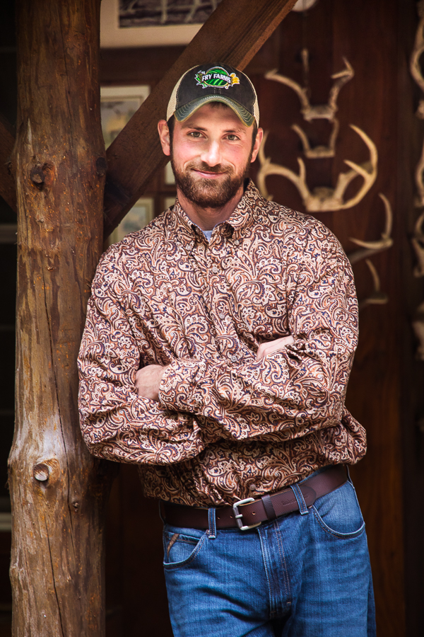 pa country wedding photographer, lisa rhinehart, photographs a traditional portrait of the groom in his unique attired and pattern button down shirt with wooden beams and antlers in the background behind him 