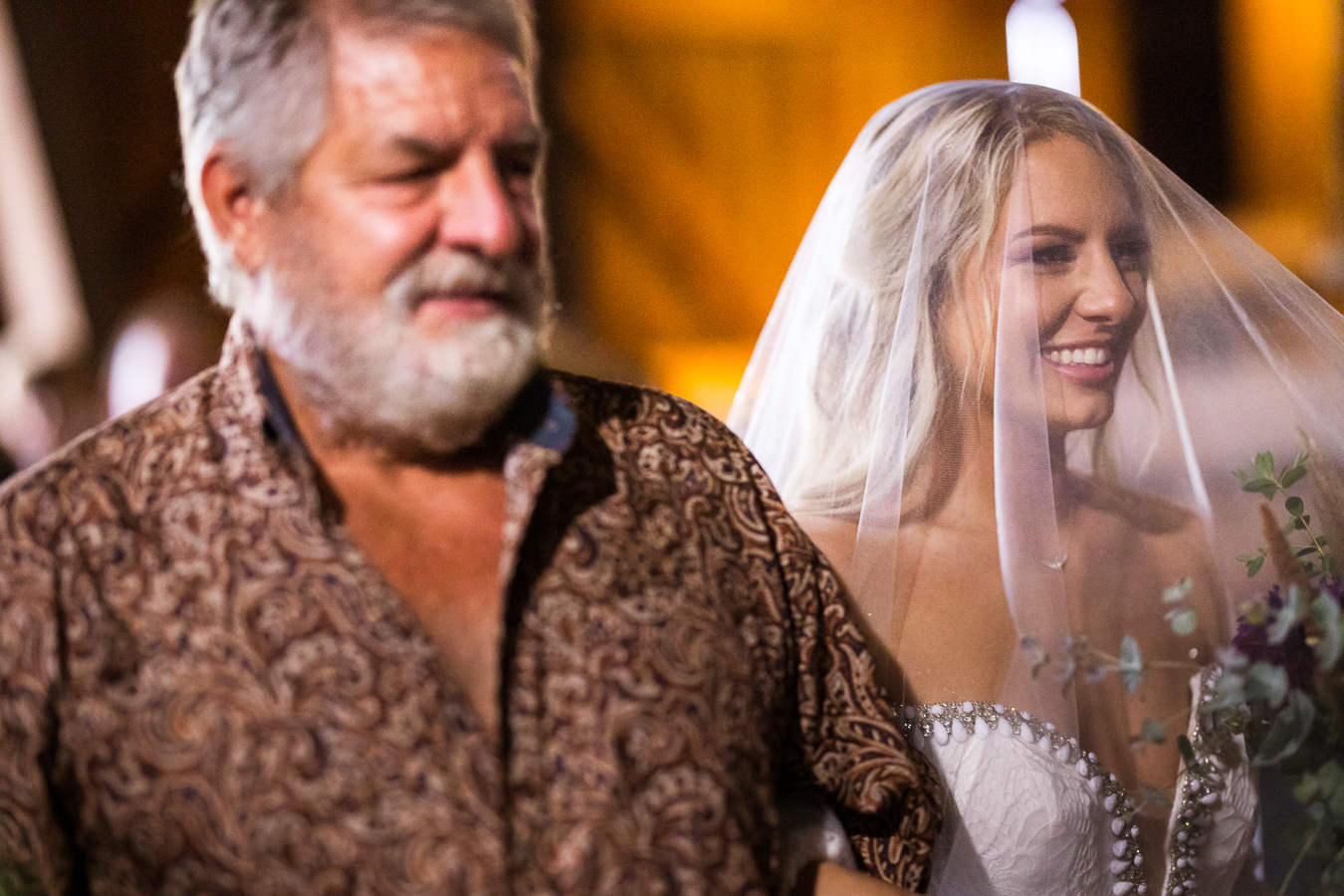 candid wedding photographer, rhinehart photography, captures this image of the bride as she smiles at her groom as her dad walks her down the aisle during this country barn wedding ceremony 