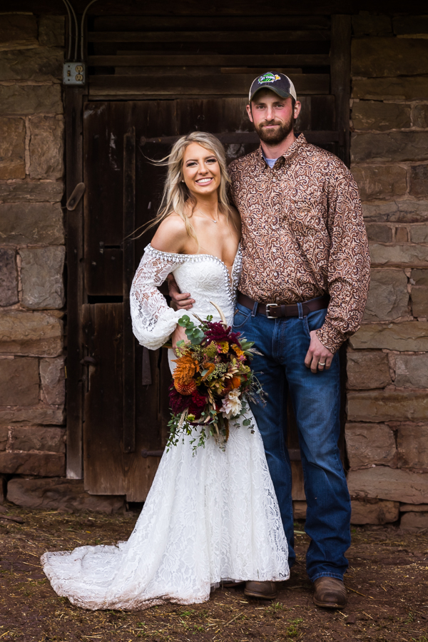 best pa wedding photographer, lisa rhinehart, captures this traditional portrait of the bride and groom as they stand beside each other after their country wedding ceremony as she holds her vibrant fall floral bouquet with antlers and the groom wears his unique patterned button up and jeans 