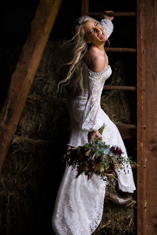 wild country wedding photographer, lisa rhinehart, captures this candid, fun image of the bride as she climbs up the ladder to the hayloft while smiling and laughing back at the camera during this barn wedding 