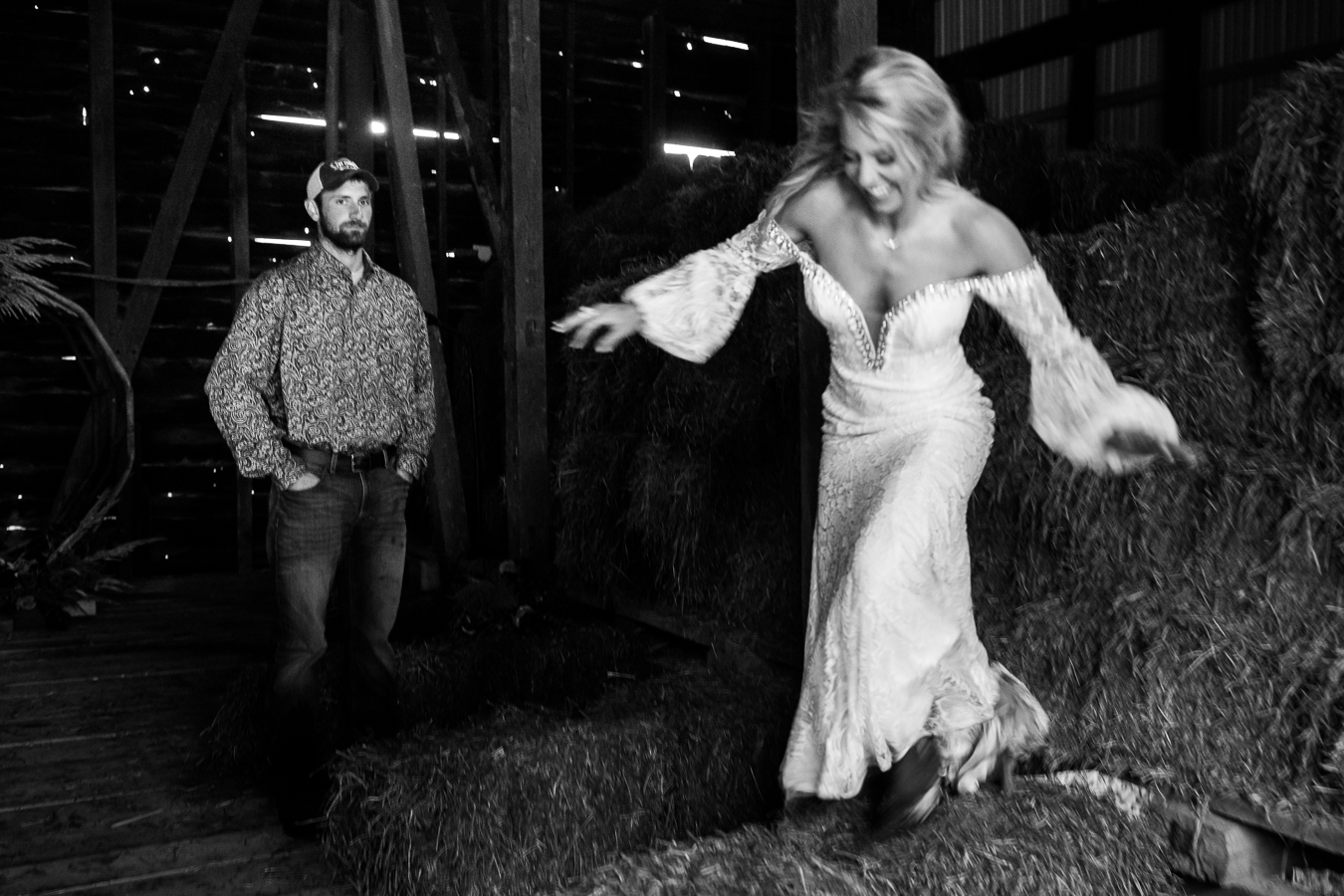 wild country wedding photographer, lisa rhinehart, captures this unique image of the bride being her outgoing, wild self and running on the hay while the groom chills in the back watching his bride