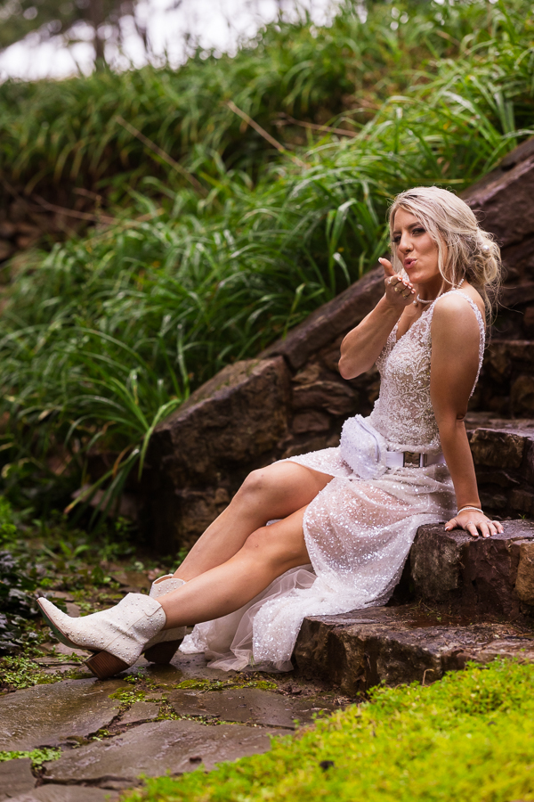 pa wedding photographer, lisa rhinehart, captures some more bridal portraits after the bride changes into her reception dress and blows a kis at the camera while sitting on the stone steps at this outdoor country wedding in halifax pa 