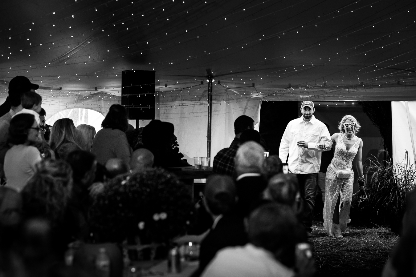 wild country wedding photographer, lisa rhinehart, captures this fun candid black and white image of the bride and groom as they enter their country inspired wedding reception wearing a white button down and fun white heart shaped glasses before they get the party started