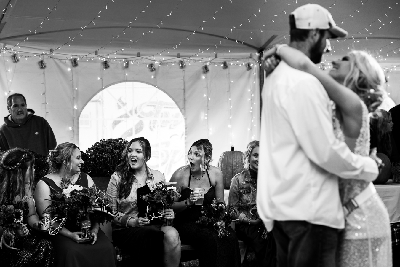 black and white image of the bride and groom as they share their first dance together as their bridesmaids smiles and gasp in joy behind them during this country inspo wedding reception 
