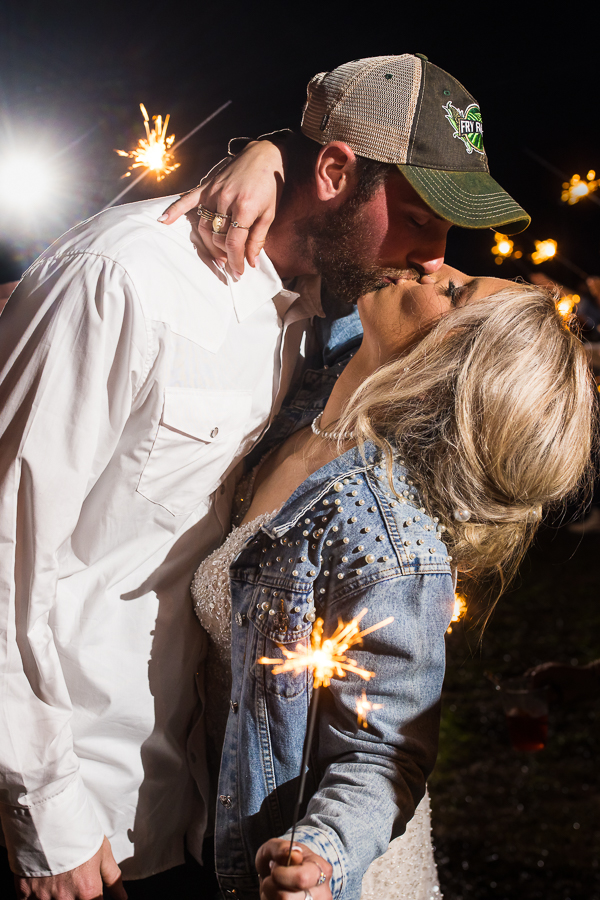 end of the night shot of the bride and groom as they kiss while sparks fly around them during the sparkler send off during this country inspired wedding day in halifax pa captured by best pa wedding photographer, lisa rhinehart