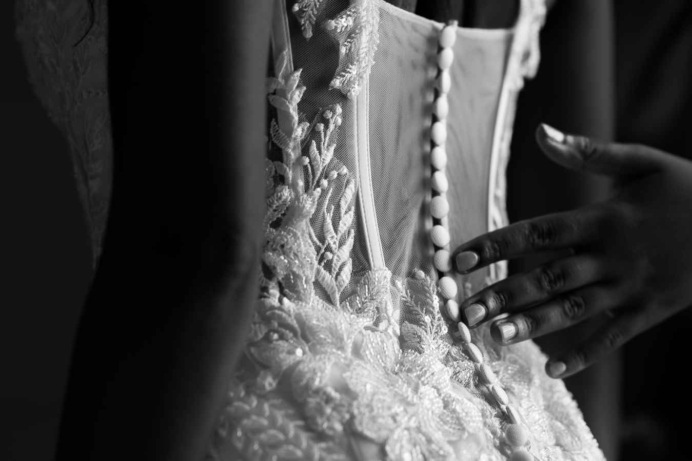 dc wedding photographer, Lisa Rhinehart, captures this black and white close up image at the st regis hotel of the back of the brides wedding gown as she is being buttoned up before her Multicultural DC Wedding at st francis hall