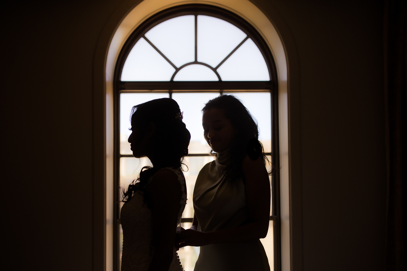 creative dc wedding photographer, Lisa Rhinehart, captures this unique silhouette of the brides wedding dress being buttoned up by her maid of honor during her wedding preparations at the st regis hotel in Washington DC