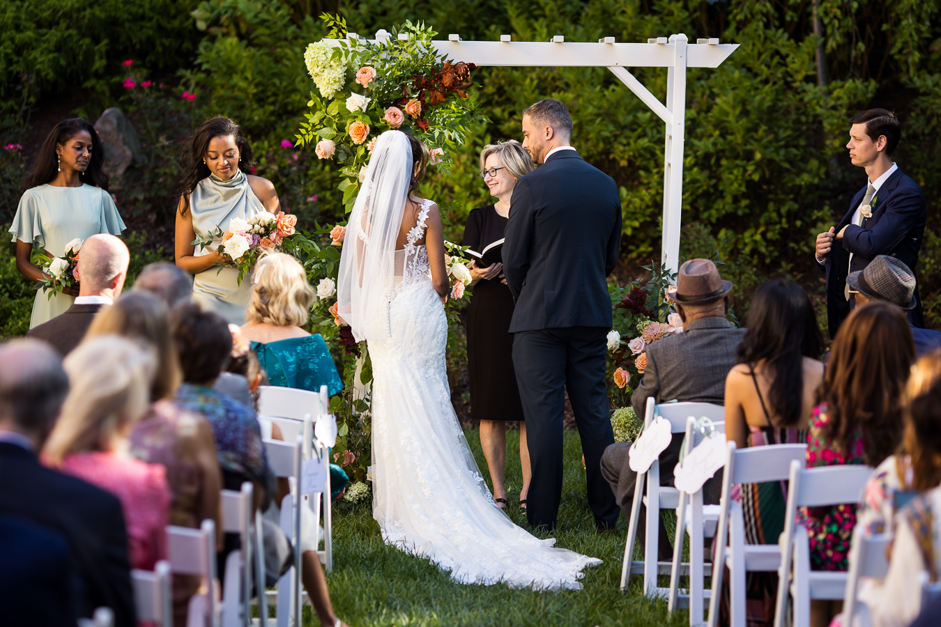 vibrant, colorful image of the bride and groom as they stand next to one another at the end of the aisle during their outdoor multicultural st francis hall wedding ceremony 
