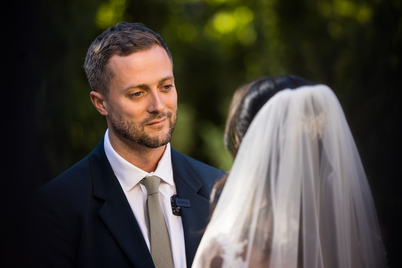 close up portrait of the groom as he stares into his Ethiopian bride's eyes with a smile during their outdoor multicultural wedding ceremony at st francis hall captured by wedding photographer, Lisa Rhinehart 