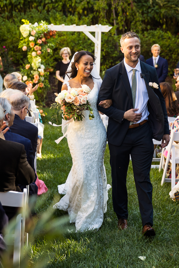 vibrant colorful image of the bride and groom as they walk down the aisle together arm in arm and smiling after getting married at st francis hall in Washington DC 