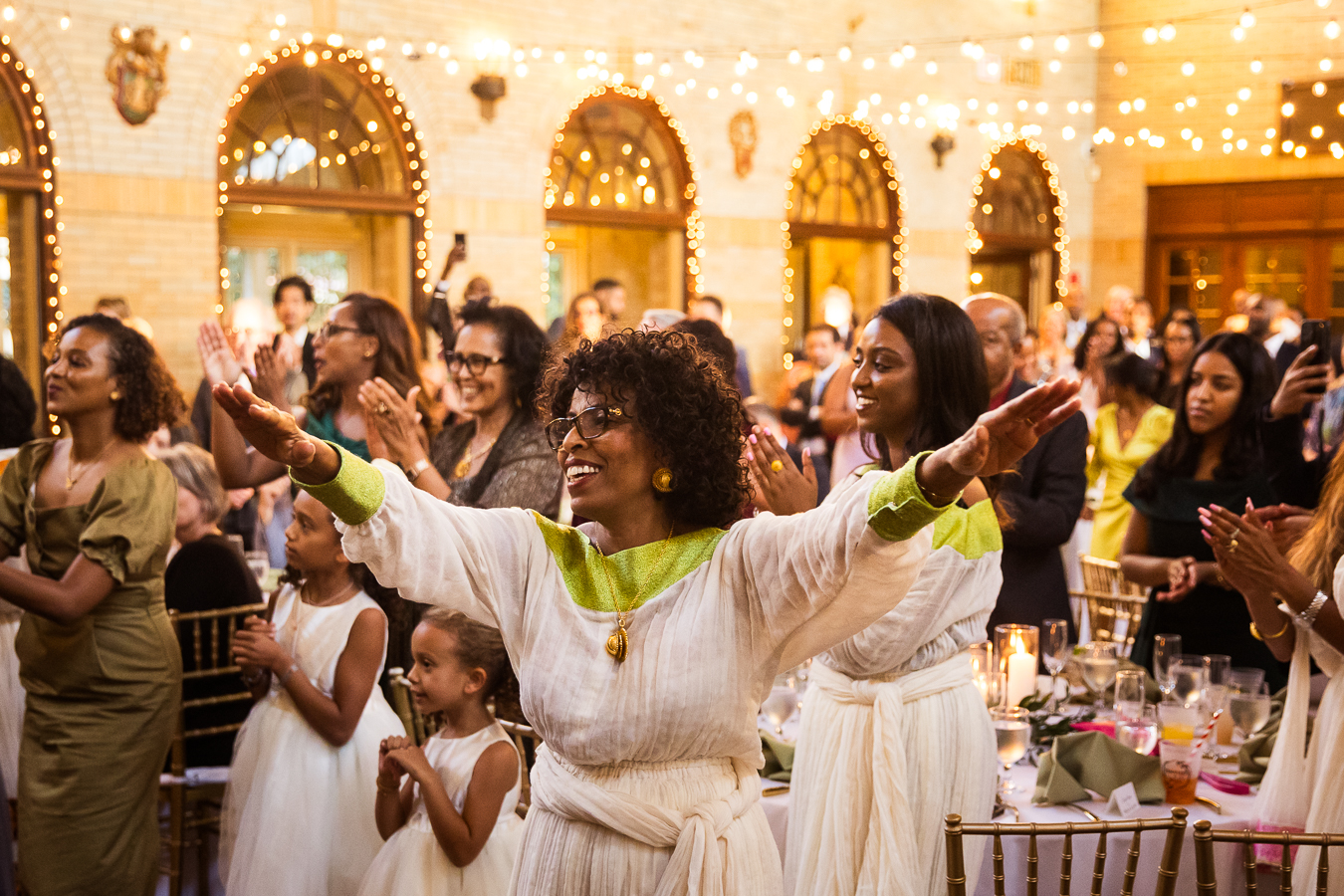 image of Ethiopian wedding guests as they cheer and clap for the groom and Ethiopian bride as they enter their Multicultural DC Wedding reception at st francis hall captured by dc wedding photographer, Lisa Rhinehart 