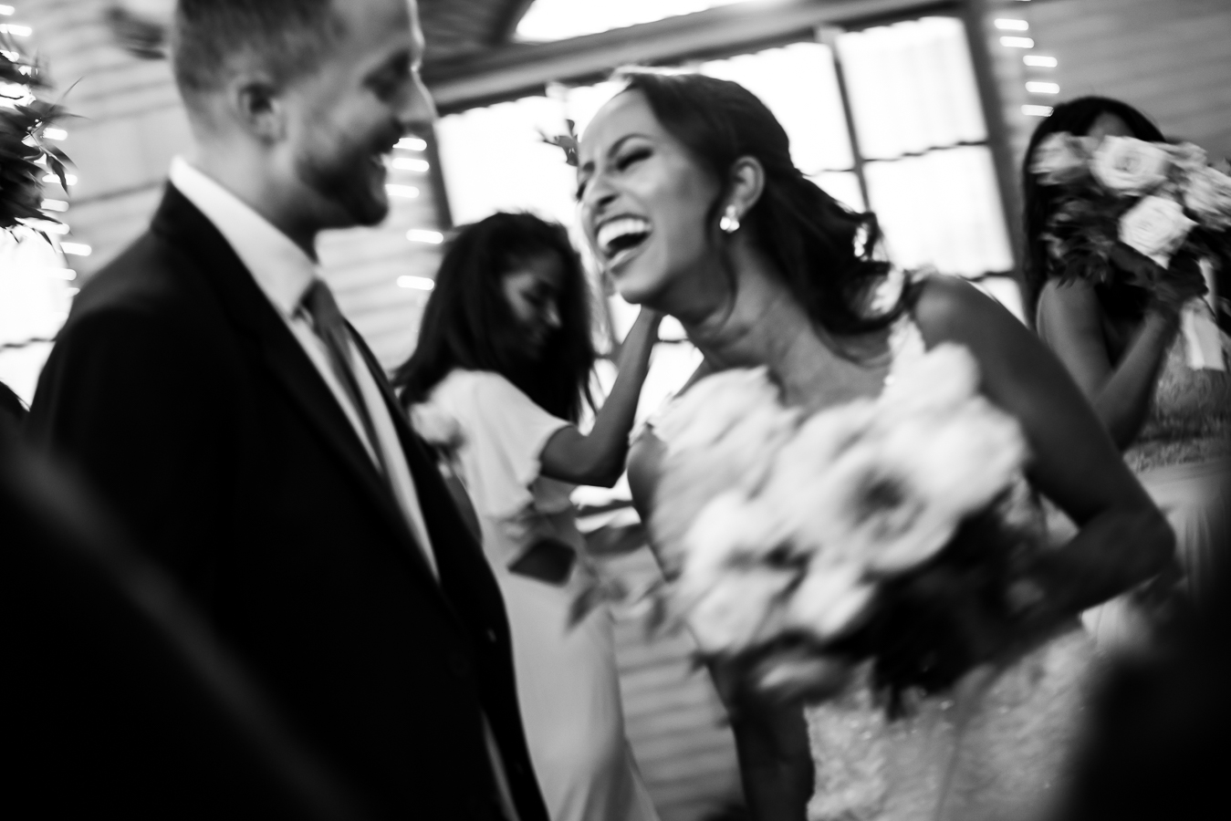black and white image of the bride and groom as they laugh with one another as their wedding party dances around them during their st Francis hall wedding reception 
