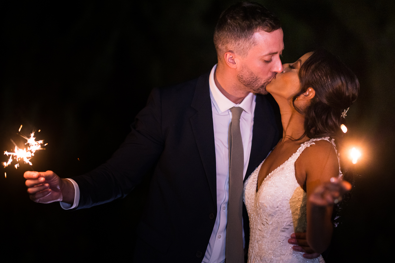 dc wedding photographer, lisa rhinehart, captures this end of the night shot of the bride and groom as they share a kiss together while holding sparklers at the end of their st francis hall multicultural dc wedding reception 