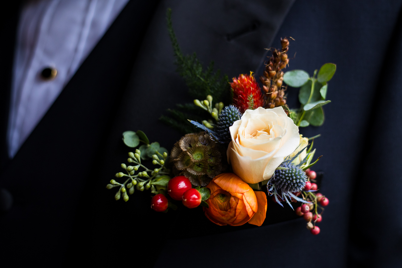 close up detail image of the grooms boutonniere with vibrant fall foliage of red, orange, blue, green and browns 