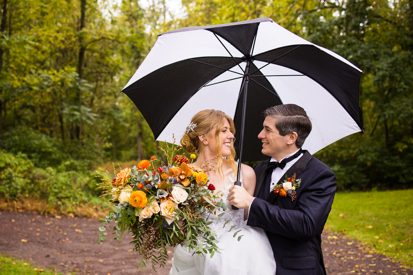 fun, unique romantic portrait of the bride and groom as they share an umbrella and walk down the paths as they smile at each other despite the rainy wedding day they are having 