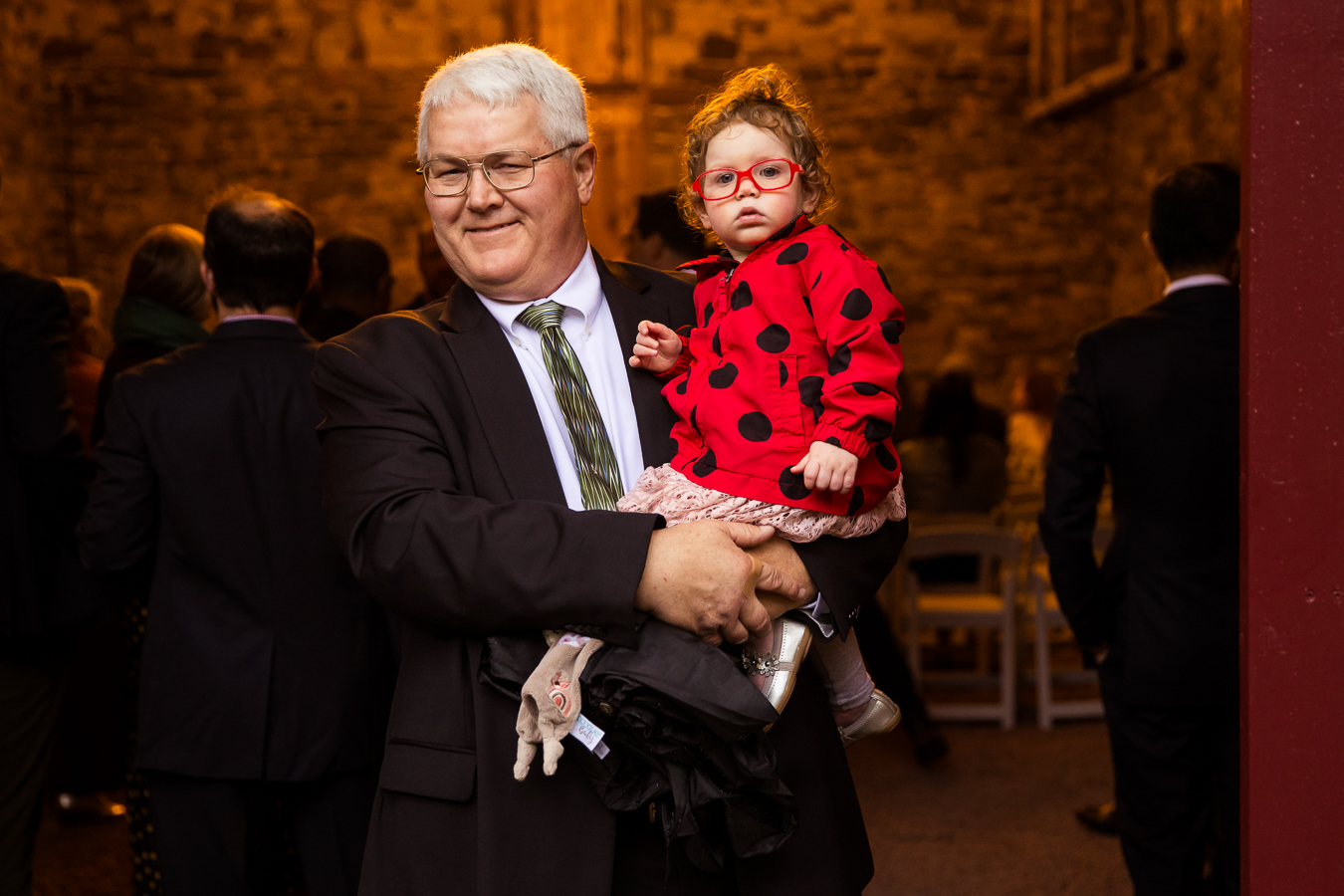 candid moment of a guest as he holds a little girl dressed in her ladybut outfit as they wait for the bride to walk down the aisle 