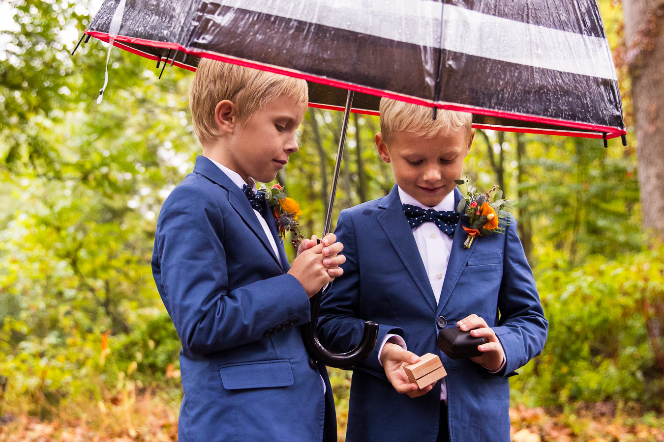 candid moment between the ring bears as they stand under the umbrellas and look at the rings before this Elizabeth Furnace Wedding ceremony in lititz pa