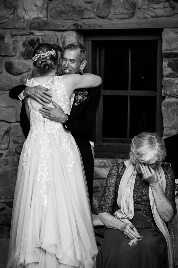 Elizabeth Furnace Wedding photographer, lisa rhinehart, captures this black and white image of the bride as she hugs her father after his speech while her mother is in the lower corner crying after hearing his speech at this indoor wedding reception 