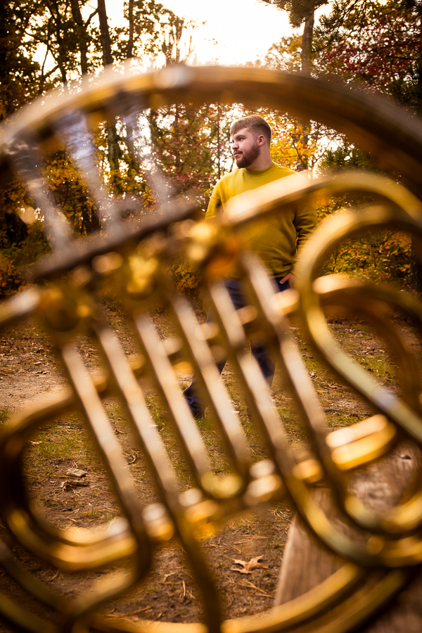 northern york senior portrait photographer, lisa rhinehart, captures this creative, unique image of this senior through his french horn as he is surrounded by the fall foliage of kings gap mansion in central pa 