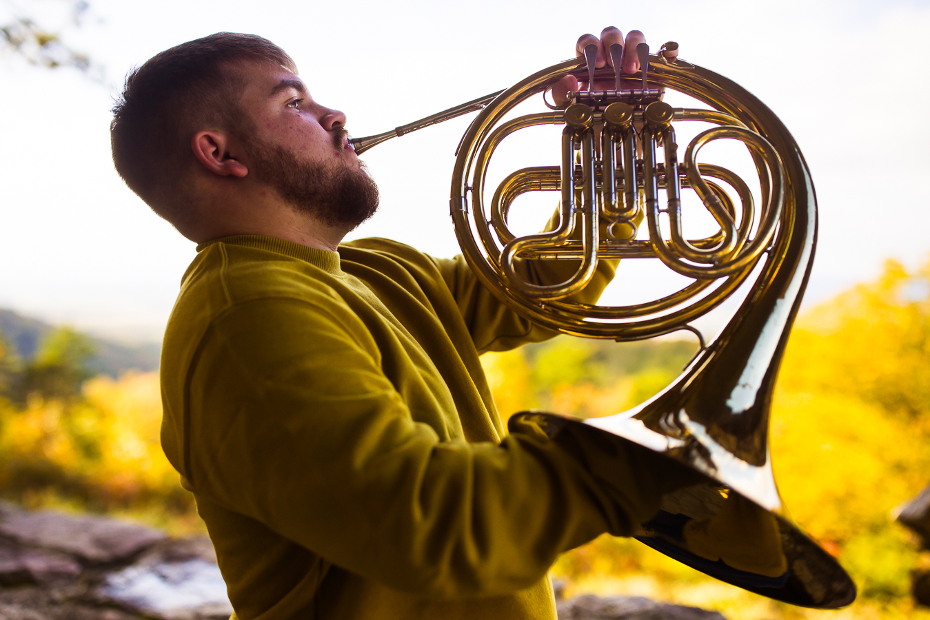 Creative portrait photographer, lisa rhinehart, captures this image of this french horn player as he shows off how he can play his instrument with cerebral palsy ontop of the mountain at kings gap mansion in central pa surrounded by the vibrant, colorful fall foliage