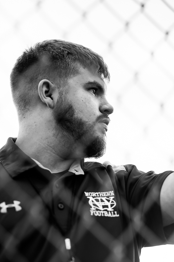 black and white image of this cerebral palsy senior as he watches through the fence as his team practices football