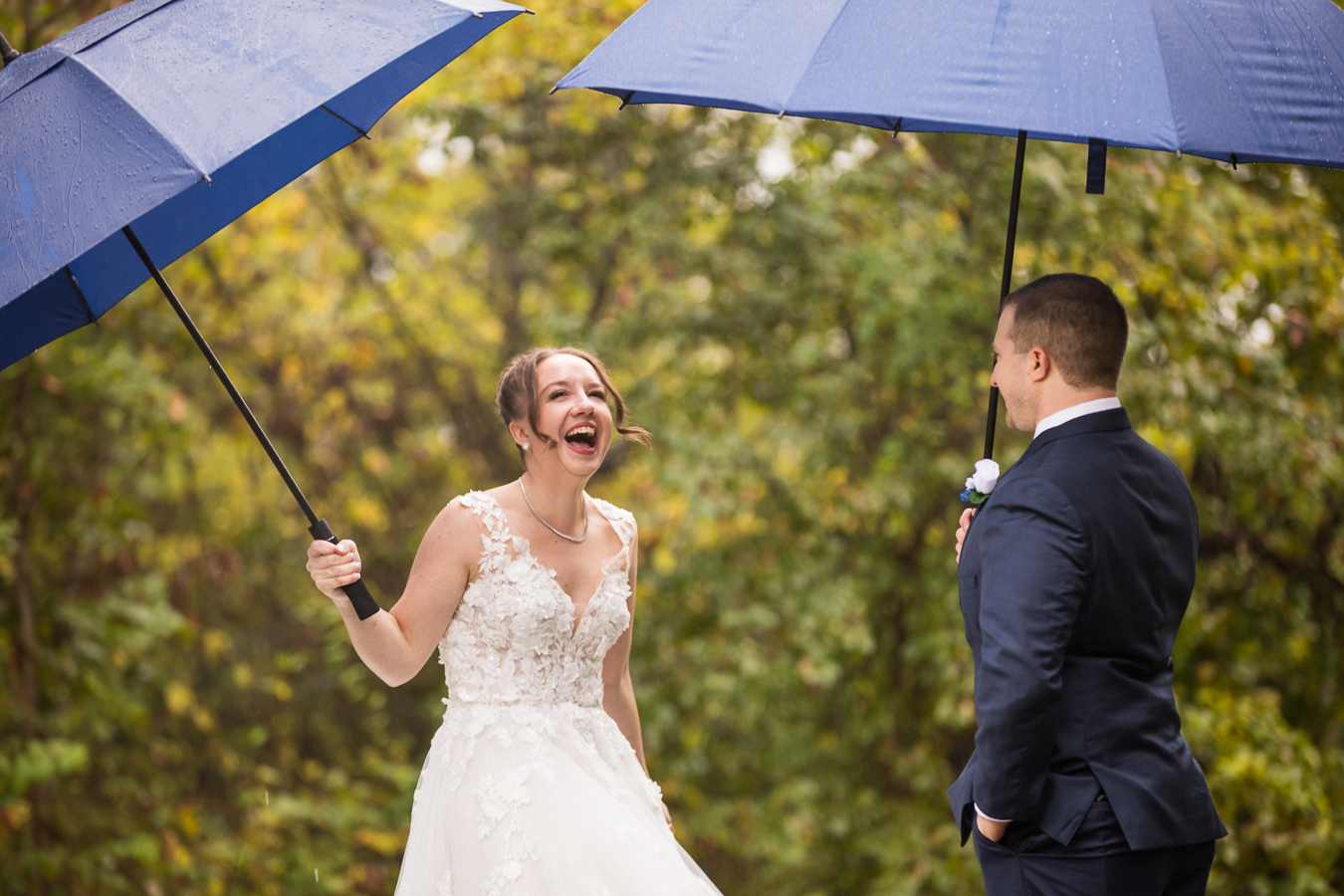 rainy day wedding first look captured by pa wedding photographer, lisa rhinehart, of the bride and groom as they smile and laugh at one another while holding large blue umbrellas during their Gettysburg battlefield first look 