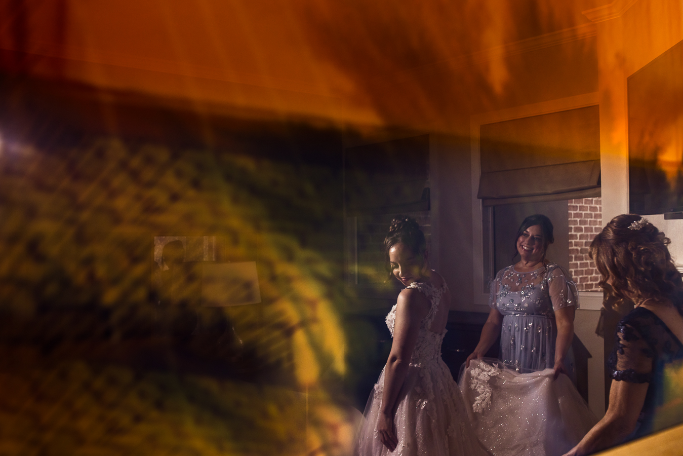 creative, unique bridal portrait of the bride as her bridesmaids help her get ready and show off her dress in this creative, vibrant reflective wedding preparation photo at Gettysburg hotel