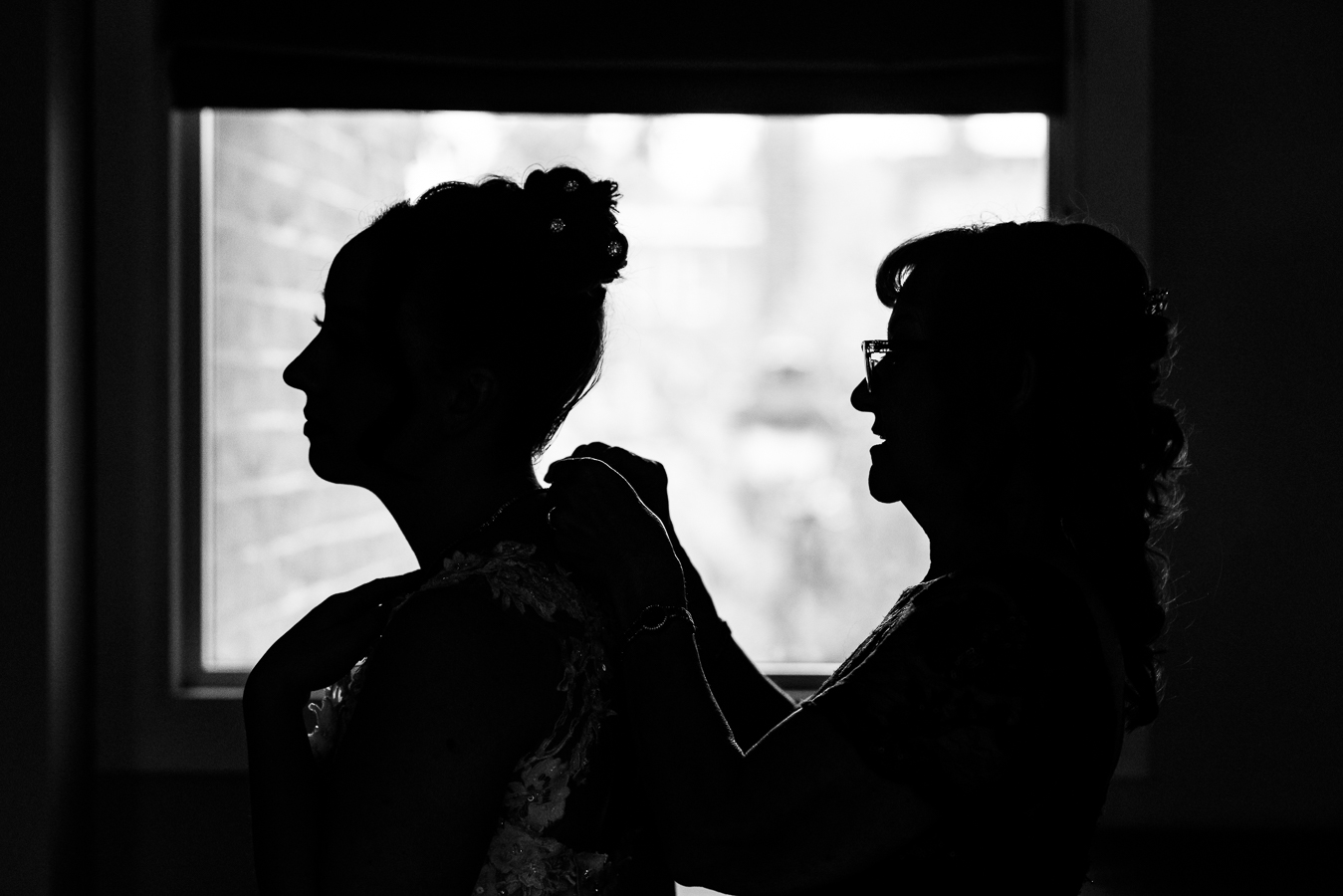 black and white silhouette of the bride as her mom helps to put her necklace on in front of this window at the Gettysburg hotel in central pa 