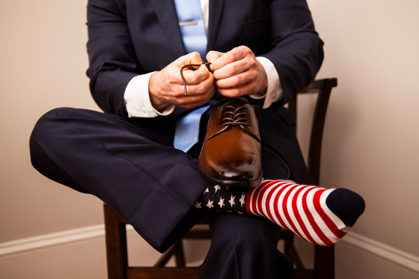 image of the groom as he unties his shoes to put them over top of his red white and blue stars and stripes socks during his wedding preparations at the Gettysburg hotel