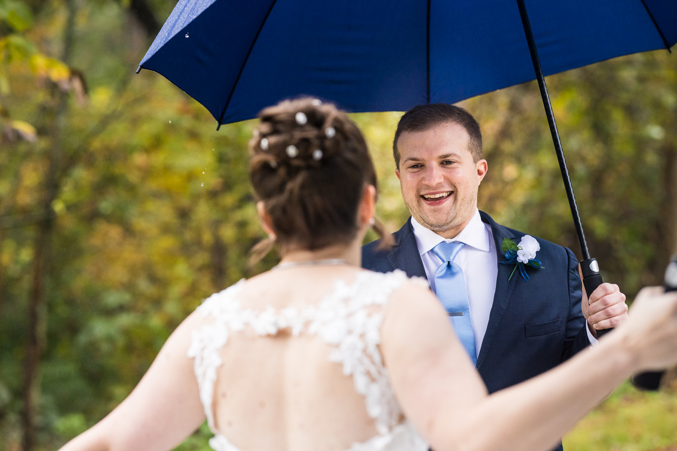 image of the groom as he smiles at his bride underneath an umbrella during this rainy day first look before their central pa wedding ceremony 