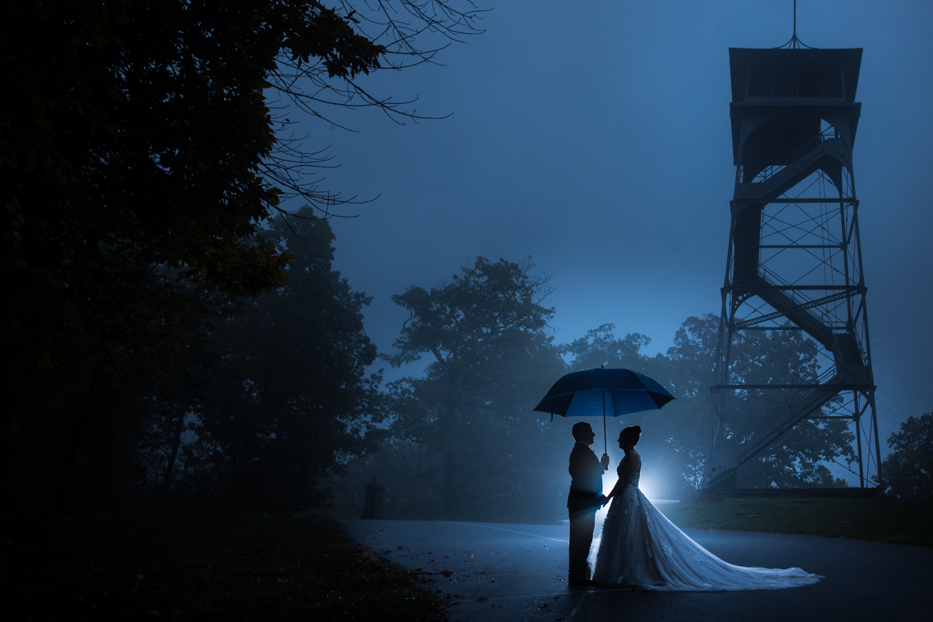creative wedding photographer, lisa rhinehart, captures this image of the bride and groom as they hold hands underneath the umbrella to avoid the rainy day as they stand beside culps hill inside of the Gettysburg battlefields as the fog surrounds them