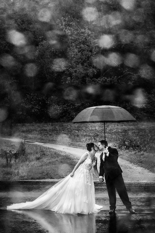 black and white image of the bride and groom as they kiss one another underneath their umbrella during their rainy day first look 