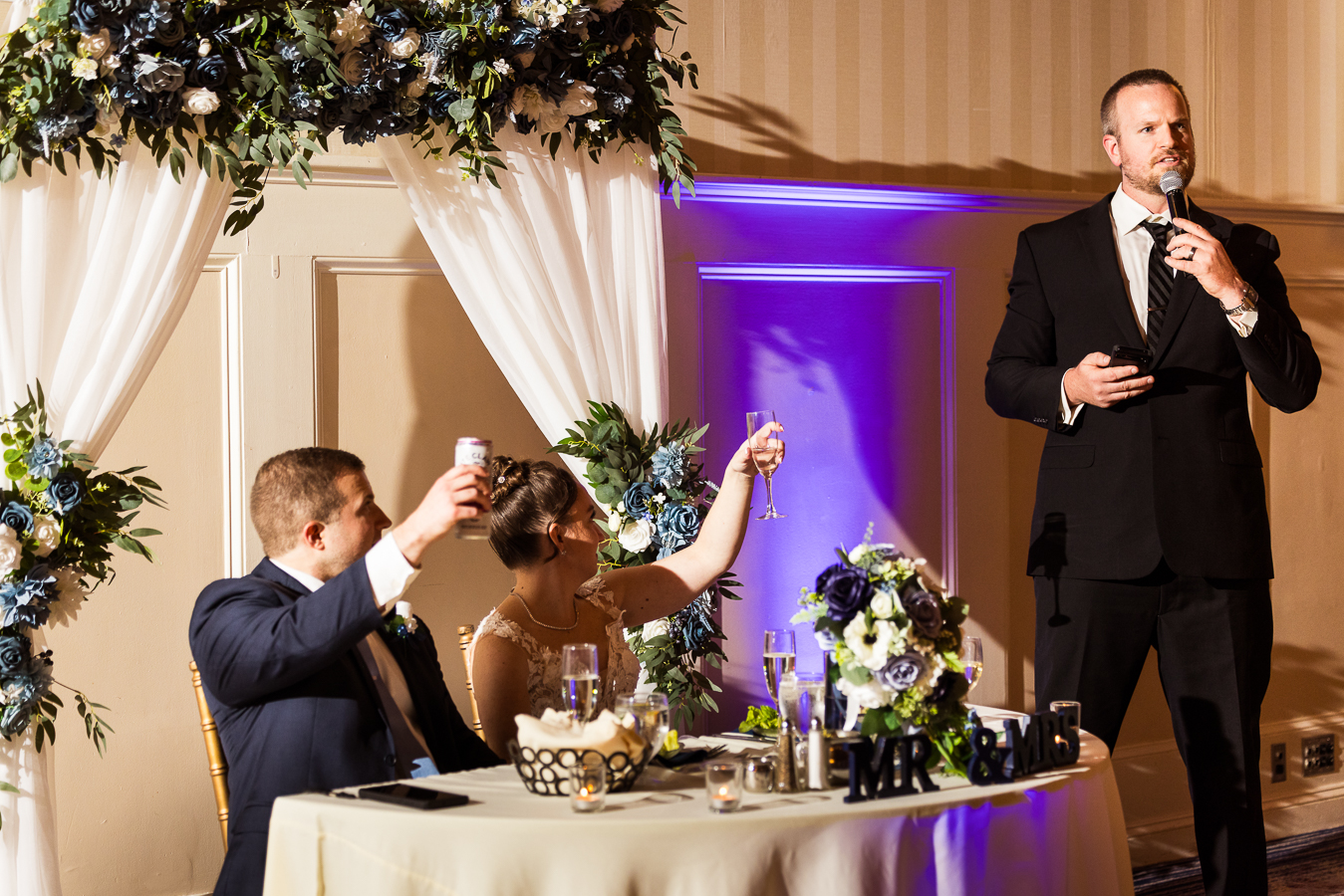image of the bride and groom as they share a toast while one of the groomsmen shares their speech during the wedding traditions portion of this Gettysburg hotel wedding reception 