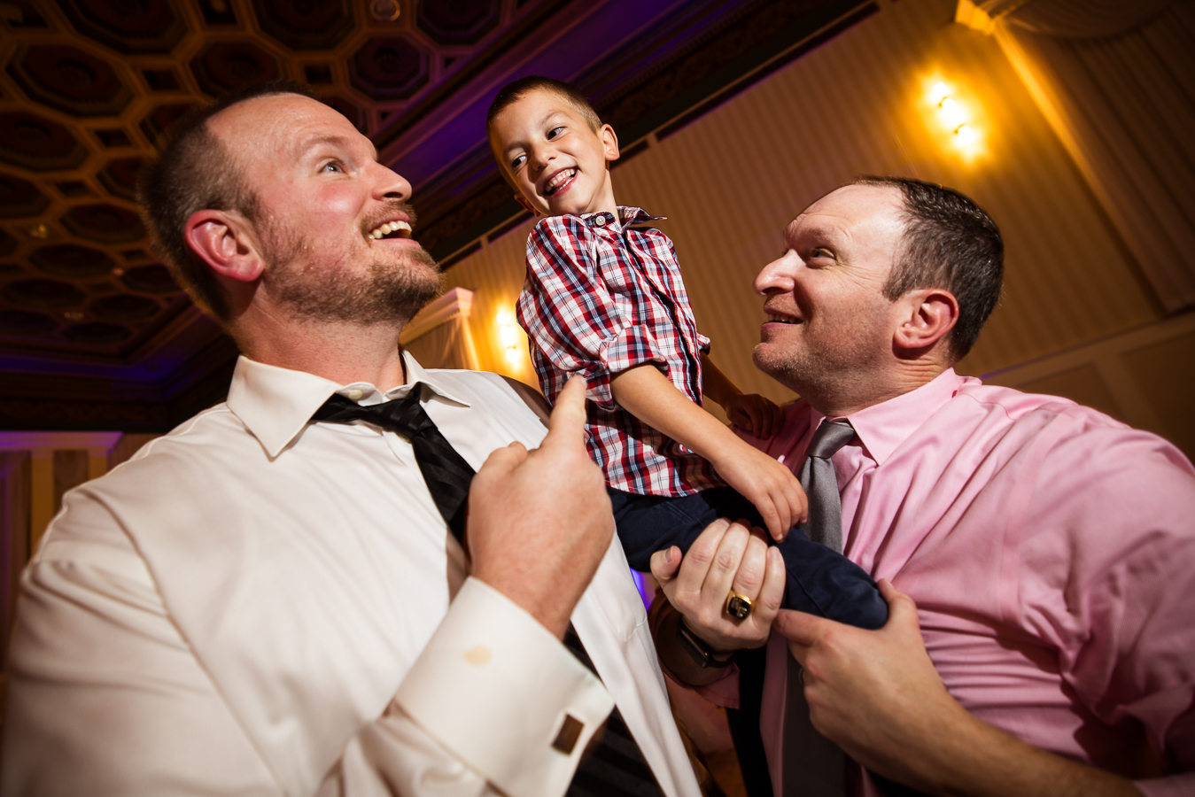 close up image guests as they hold a little boy up into the air while laughing and smiling during this fun Gettysburg wedding reception 