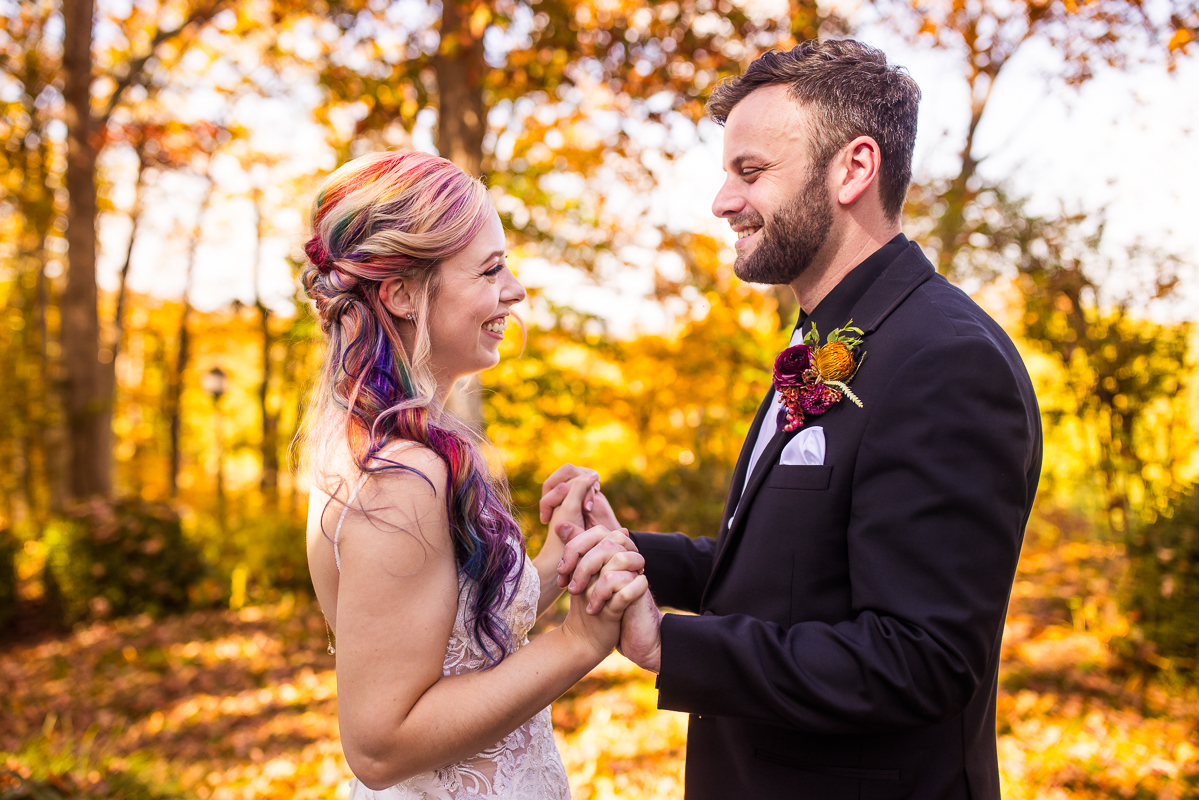 Murray Hill wedding photographer, lisa rhinehart, captures this vibrant, colorful outdoor fall wedding portraits of this bride and groom as they hold hands and smile at one another surrounded by the fall foliage of Murray Hill Virginia