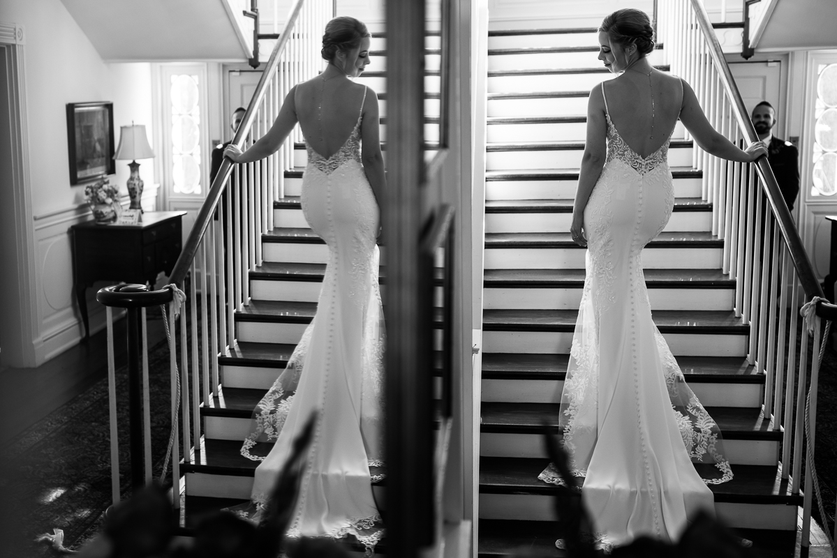 creative virginia wedding photographer, lisa rhinehart, captures this black and white image of the bride as she shows off the back of her dress while standing on the staircase in this virginia wedding venue in Leesburg va
