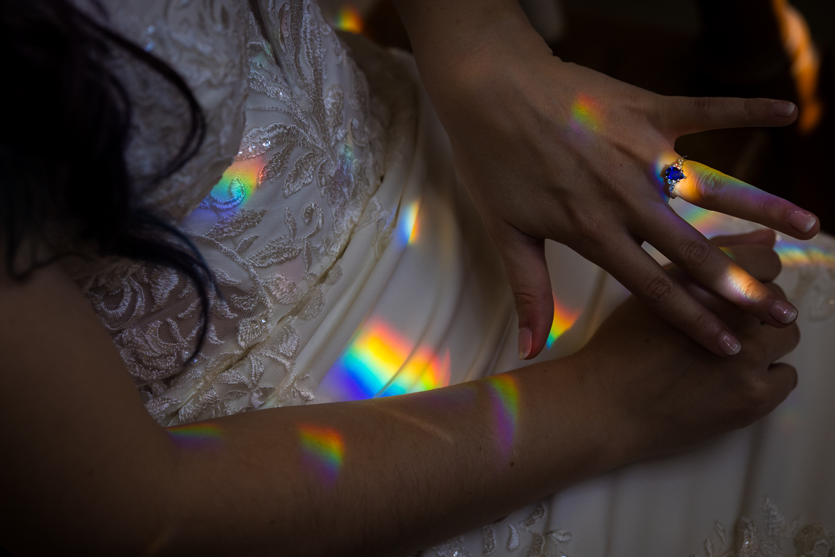 creative wedding photographer, lisa rhinehart, captures the vibrant, colorful rainbows that are reflected on the brides wedding dress as she shows off her sapphine wedding ring on her hand during her wedding preparations