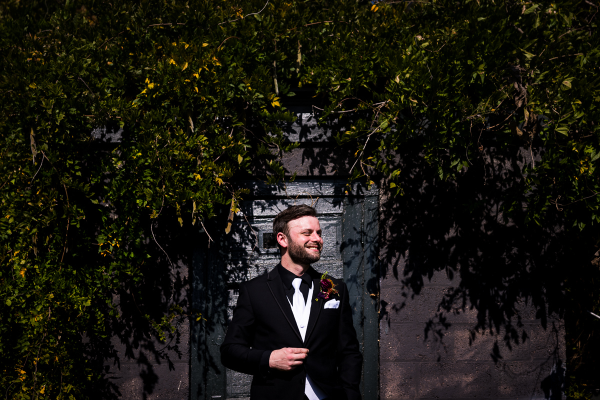 outdoor portrait of the groom as he smiles off into the distance surrounded by green vines in Leesburg va 