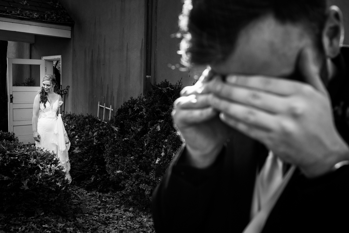 black and white image of the groom as he covers his eyes as the bride walks out to him for their outdoor fall first look in Leesburg va