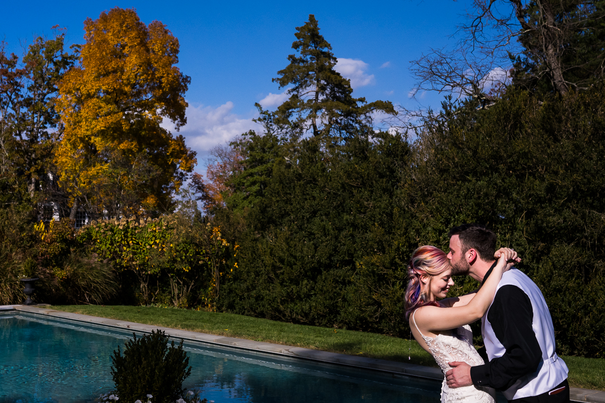 leesburg va wedding photographer, lisa rhinehart, captures this vibrant, colorful image of the bride and groom as they kiss one another beside the reflecting pool while surrounded by the vibrant fall foliage of Virginia 