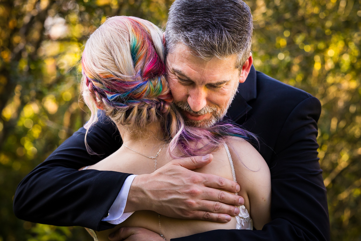 candid image of the bride with her rainbow hair as she hugs her dad outside of Murray hill before the outdoor wedding ceremony in Leesburg va