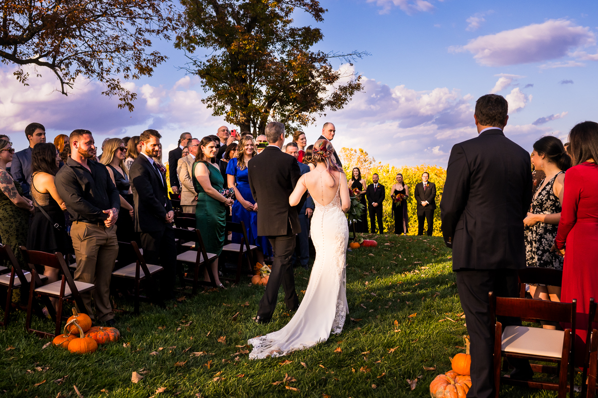 Murray Hill wedding photographer, lisa rhinehart, captures this vibrant, colorful image of the bride as she walks down the aisle with her dad to her wedding ceremony that overlooks the Potomac river in Leesburg va 