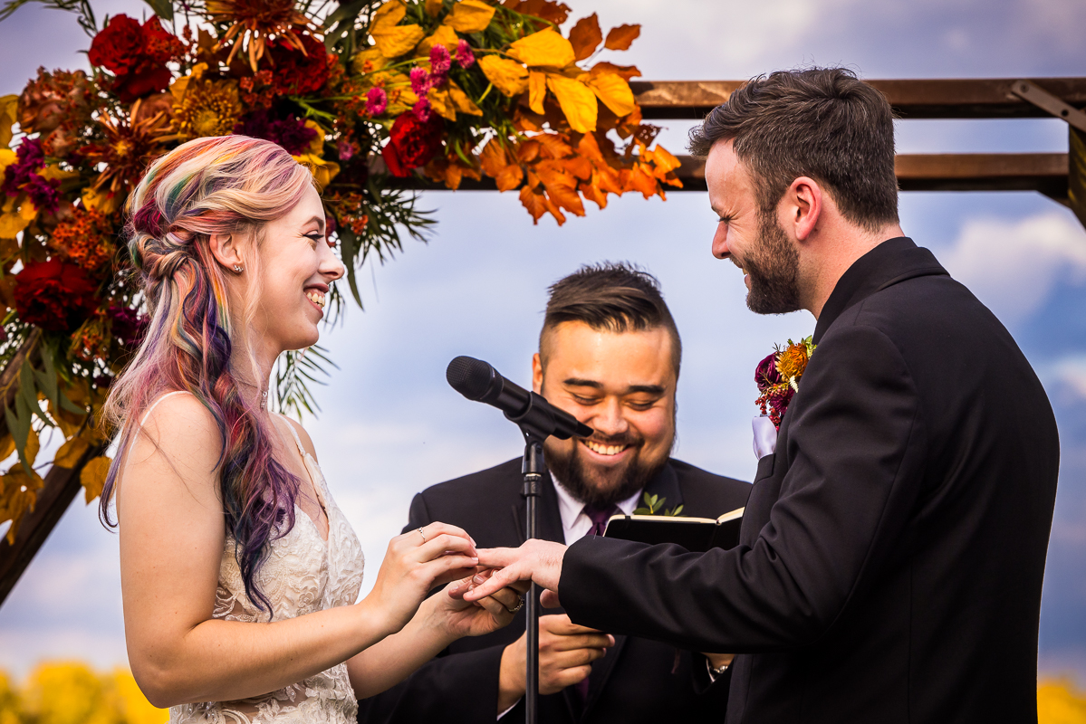 Close up image of the bride and groom as they place the rings on each others hands during this outdoor fall wedding ceremony beside the Potomac river in Leesburg va 