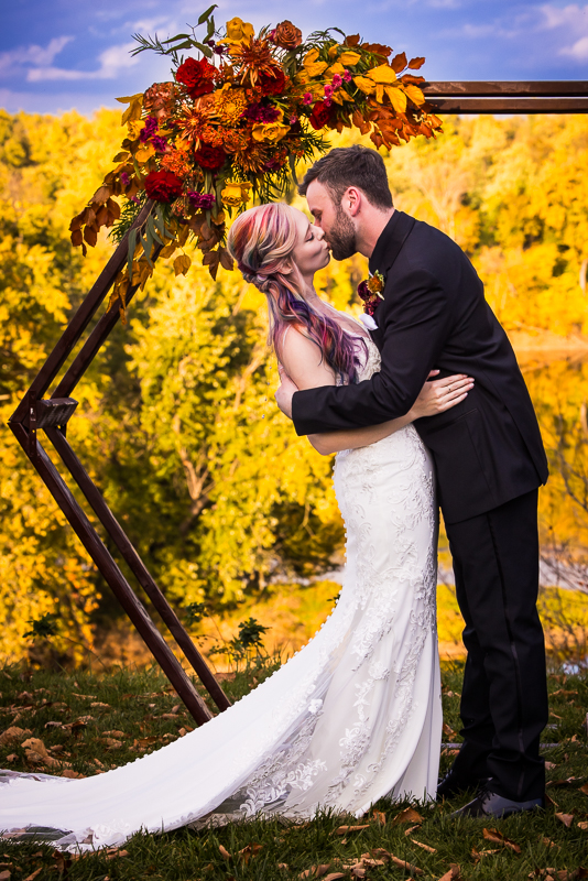 traditional portrait of the bride and groom as they share their first kiss at the end of the wedding ceremony with the vibrant yellow fall foliage in the background behind them in Virginia 