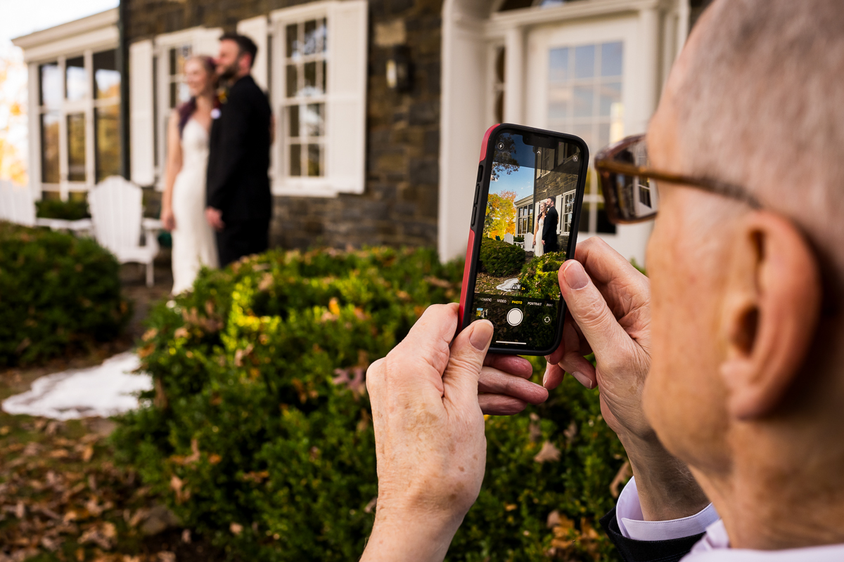 candid virginia wedding photographer, lisa rhinehart, captures this candid moment of the bride and groom as they get a portrait taken together while the grandfather captures the same moment on his cellphone 